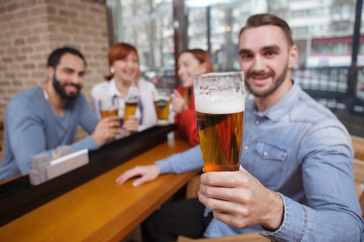 Selective focus on a glass of delicious craft beer in the hand of a cheerful man. Group of friends celebrating at beer pub