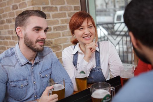 Young beautiful happy woman enjoying drinking beer with her friends at the pub