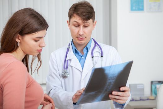 Mature doctor examining x-ray scan of his female patient during medical appointment