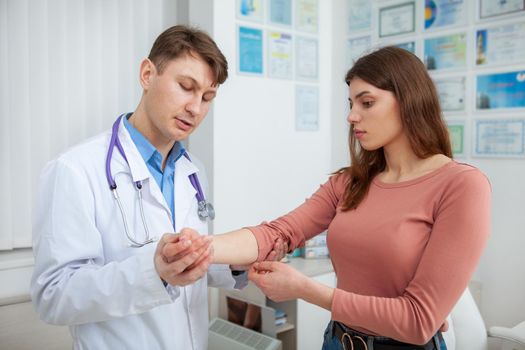 Young beautiful woman having her injured arm examined by experienced doctor at the hospital