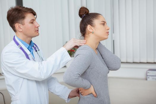 Young woman suffering from back pain visiting doctor at the hospital. CHiropractor examining aching back of a female patient