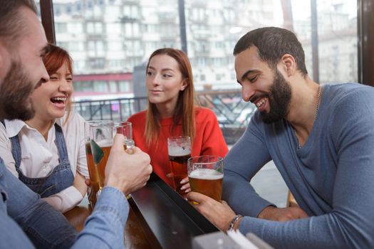 Happy young people enjoying relaxing together at beer pub. Group of friends laughing over a joke while drinking beer