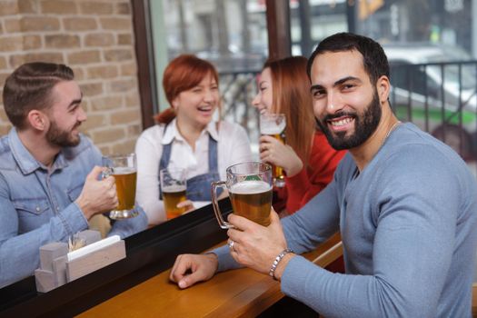 Happy bearded man smiling to the camera while drinking beer with his friends at the pub