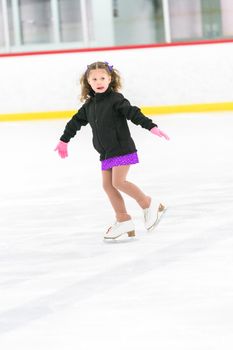 Little girl practicing figure skating on an indoor ice skating rink.