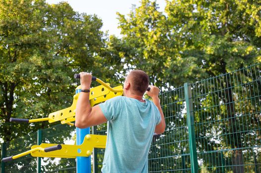 A man is exercising on the street. Training for beautiful hands. Opening gym outdoors on the sports ground in a green park