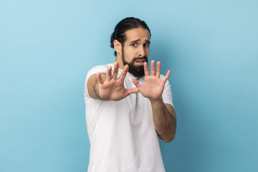 Portrait of nervous embarrassed man with beard wearing white T-shirt feels scared reacts on something looks anxious, having anxiety or being troubled. Indoor studio shot isolated on blue background.