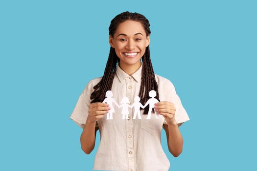 Portrait of happy woman with black dreadlocks holding paper chain people in hands, concept of happy family, parenthood, childhood, wearing white shirt. Indoor studio shot isolated on blue background.