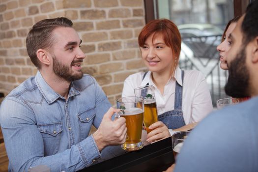 Handsome young man talking to his friends while drinking beer together. Group of cheerful people having drinks at the bar