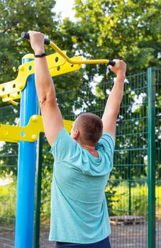 A man is exercising on the street. Opening gym outdoors on the sports ground in a green park