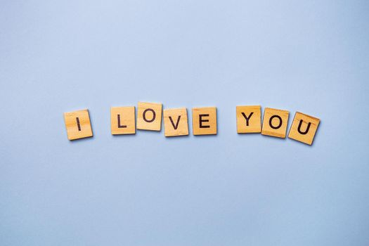 Inscription I love you in wooden square letters on a light blue background. Ready postcard, banner, place for an inscription