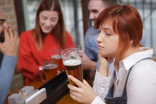 Young woman looking upset, drinking beer, while her female friend flirting with med on background. Jealousy, loneliness concept