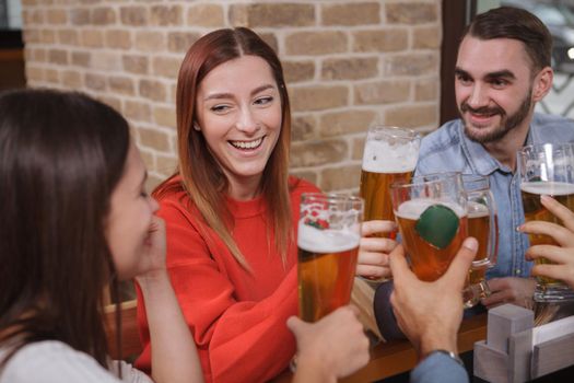 Lovely young woman laughing with her friends while drinking beer at the pub. Communication, celebration concept
