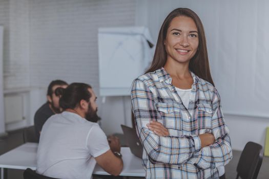 Charming businesswoman smiling ot the camera, her creative business team working on the background. Entrepreneurship, female equality, emancipation concept