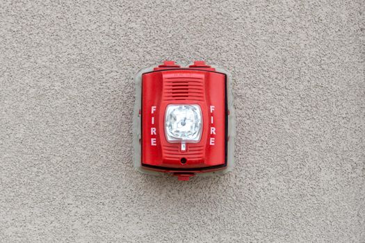 Red fire alarm siren with flashing light strobe isolated on gray cement wall outdoor. Fire safety
