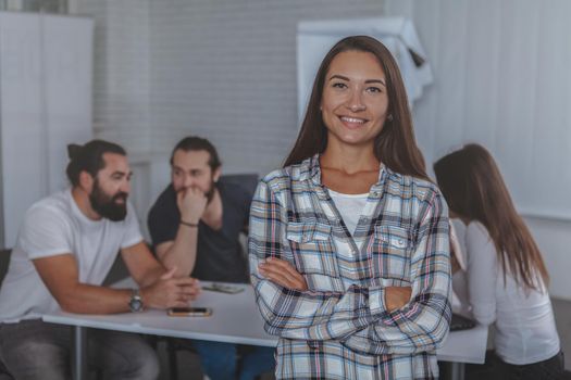 Happy young female entrepreneur posing proudly in front of her business team on the background, copy space. Successful businesswoman at the office