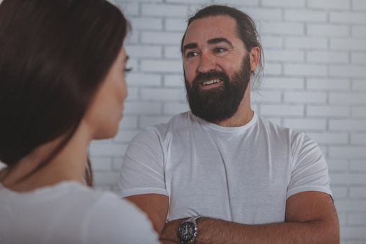 Handsome cheerful mature businessman smiling joyfully, talking to his female colleague. Happy bearded man enjoying chatting to his female friend at work