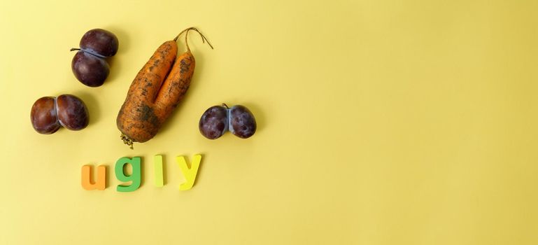 Ugly plums and carrot. Ugly fruit. Funny food. Trendy ugly food concept. Yellow bacground. Copy space