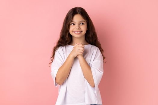 Portrait of smiling happy little girl wearing white T-shirt thinking, dreaming with joyous smiling face, pleasant fantasy, positive hopes. Indoor studio shot isolated on pink background.