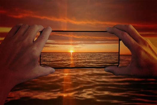 The girl photographs the sunset on the sea on a smartphone. Hands and smartphone close-up.