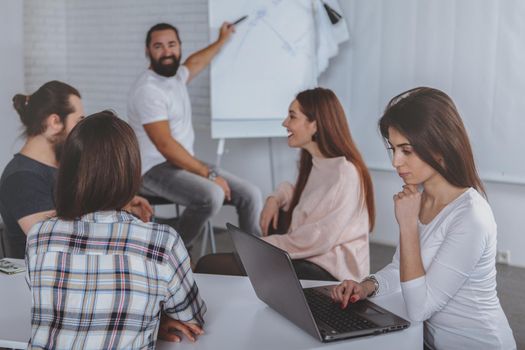 Mature bearded man smiling, talking to his creative team during business meeting. Handsome businessman leading brainstorming session with his co-workers. Ideas, leadership concept