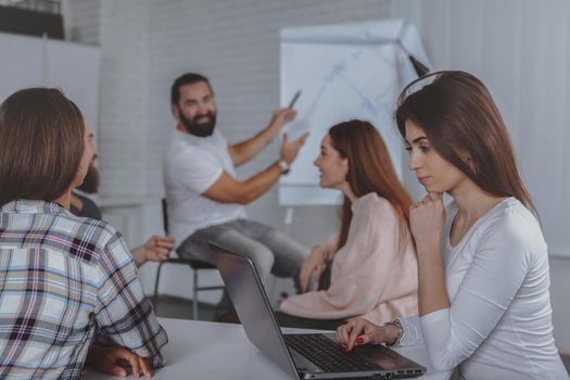 Beautiful woman using her laptop duing business meeting with colleagues at the office. Bearded mature businessman leading meeting of creative team of designers