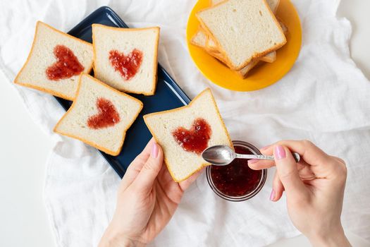 The girl makes a toast on which the heart is made of jam. Surprise breakfast concept in bed. Romance for St. Valentine's Day