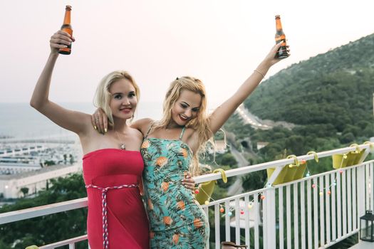 carefree young girls toasting with beers, enjoying and having fun at a private party on the outdoor terrace, leisure happiness and friendship concept, copy space for text