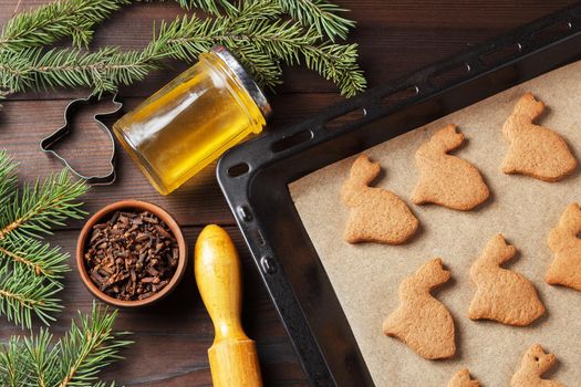 Ready-made Christmas cookies in the form of a rabbit on a baking sheet on a wooden table decorated with Christmas tree branches, with a jar of honey and cloves. Symbol of 2023
