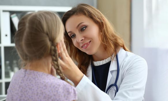 Female doctor checks throat of little girl in medical office. Children ENT diseases symptoms and treatment concept