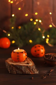 A tangerine candlestick on a wooden stand on a table decorated with fir branches and Christmas lights. Handmade.copy space. Vertical photo