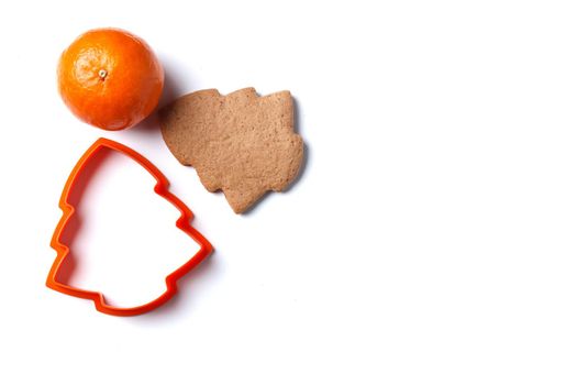 Ready-made Christmas cookies in the form of a Christmas tree with a cookie cutter and a tangerine isolated on a white background. copy space.