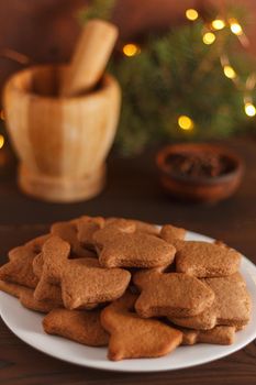 Ready-made Christmas cookies in the form of a rabbit on a white plate, on a wooden table decorated with Christmas tree branches and lights. Symbol of 2023. Vertical photo