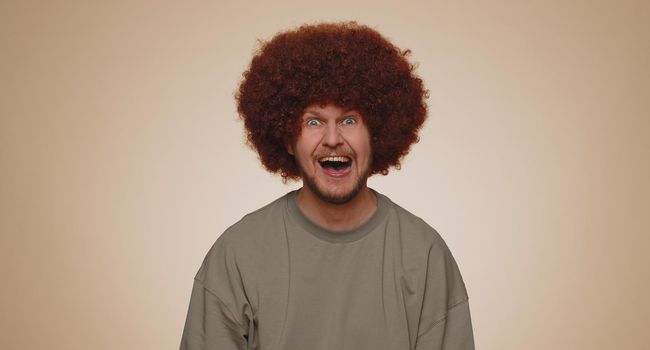 Joyful man with lush hairstyle laughing out loud after hearing ridiculous anecdote, funny joke, feeling carefree amused, positive people lifestyle. Young guy boy isolated on beige studio background