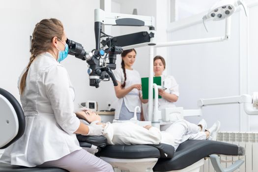 Female dentist using dental microscope treating patient teeth at dental clinic office. Medicine, dentistry and health care concept