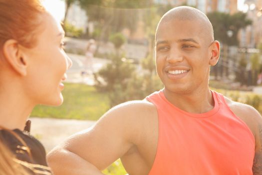 Cropped close up of a handsome African man smiling joyfully, enjoying resting outdoors with his girlfriend after working out. Cheerful athletic man and his girlfriend relaxing outdoors in the park after morning workout