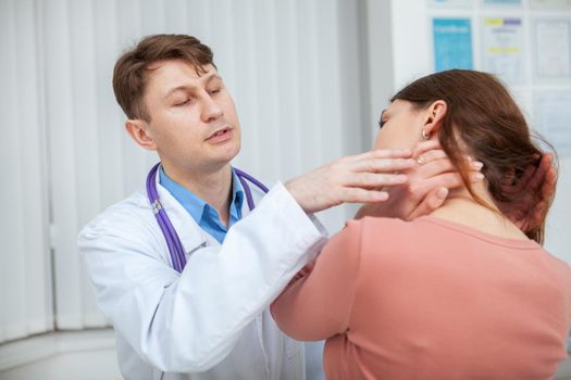 Experienced male doctor examining neck of his female patient. Woman with aching neck visiting doctor