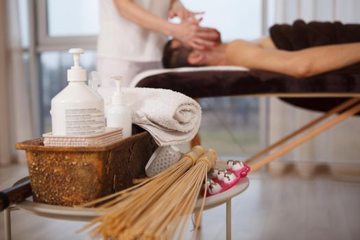 Selective focus on massage tools and oils, man getting relaxing massage by spa therapist on background