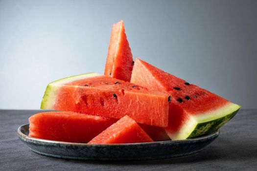 Sliced pieces of ripe sweet watermelon lie on a gray ceramic plate on a gray surface. Selective focus.