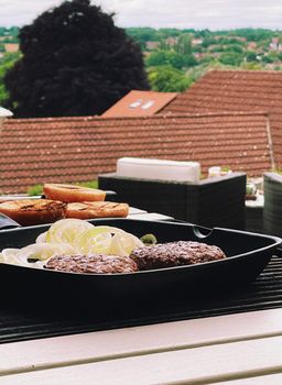 Cooking minced beef burger on cast iron grill skillet outdoors, red meat on frying pan, grilling food in the garden, English countryside living concept