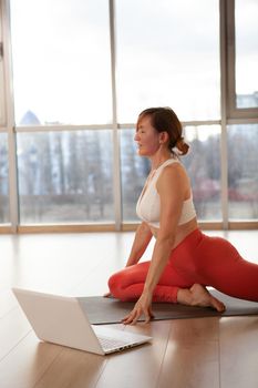 Vertical shot of a mature woman exercising with online yoga class on her laptop