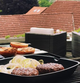 Cooking minced beef burger on cast iron grill skillet outdoors, red meat on frying pan, grilling food in the garden, English countryside living concept