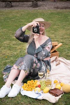 a young woman in a long dress and straw hat is resting on a picnic with fruits, cheese plate and champagne, rest from worries and household chores parks and recreation areas,.High quality photo