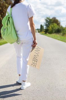 A beautiful girl with a backpack on her shoulder holds a sign with the inscription anywhere. Hitchhiking, adventure