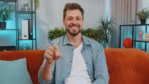 Hey, you. Portrait of adult man smiling excitedly and pointing to camera, choosing lucky winner, indicating to awesome you, inviting, approve. Young guy at modern home apartment living room on couch