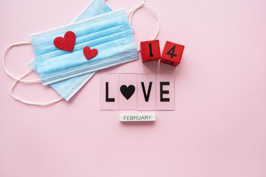 Valentine's Day celebration concept. Wooden cubes 14 February on a pink background. The heart lies on medical masks, the fight against coronavirus