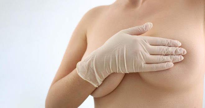 Woman breasts covered with hands in rubber gloves closeup. Mammoplasty and plastic surgery and cosmetology clinic concept