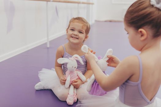 Happy little cute girl wearing tutu and leotard laughing joyfully, enjoying ballet lesson at dance school. Adorable little ballerinas resting after exercising and dancing, copy space