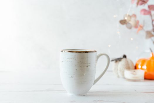 Details of Still life, cup of tea or coffee, pumpkins, candle, brunch with leaves on white table background, home decor in a cozy house. Autumn weekend concept. Fallen leaves and home decoration