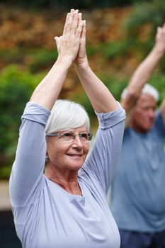 Improving her health and overall wellbeing. a senior woman doing yoga with her husband outdoors