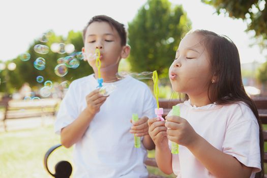 Happy cute little kids blowing bubbles outdoors in the park. Lovely Asian children having fun, blowing bubbles. Livestyle, carefree childhood concept